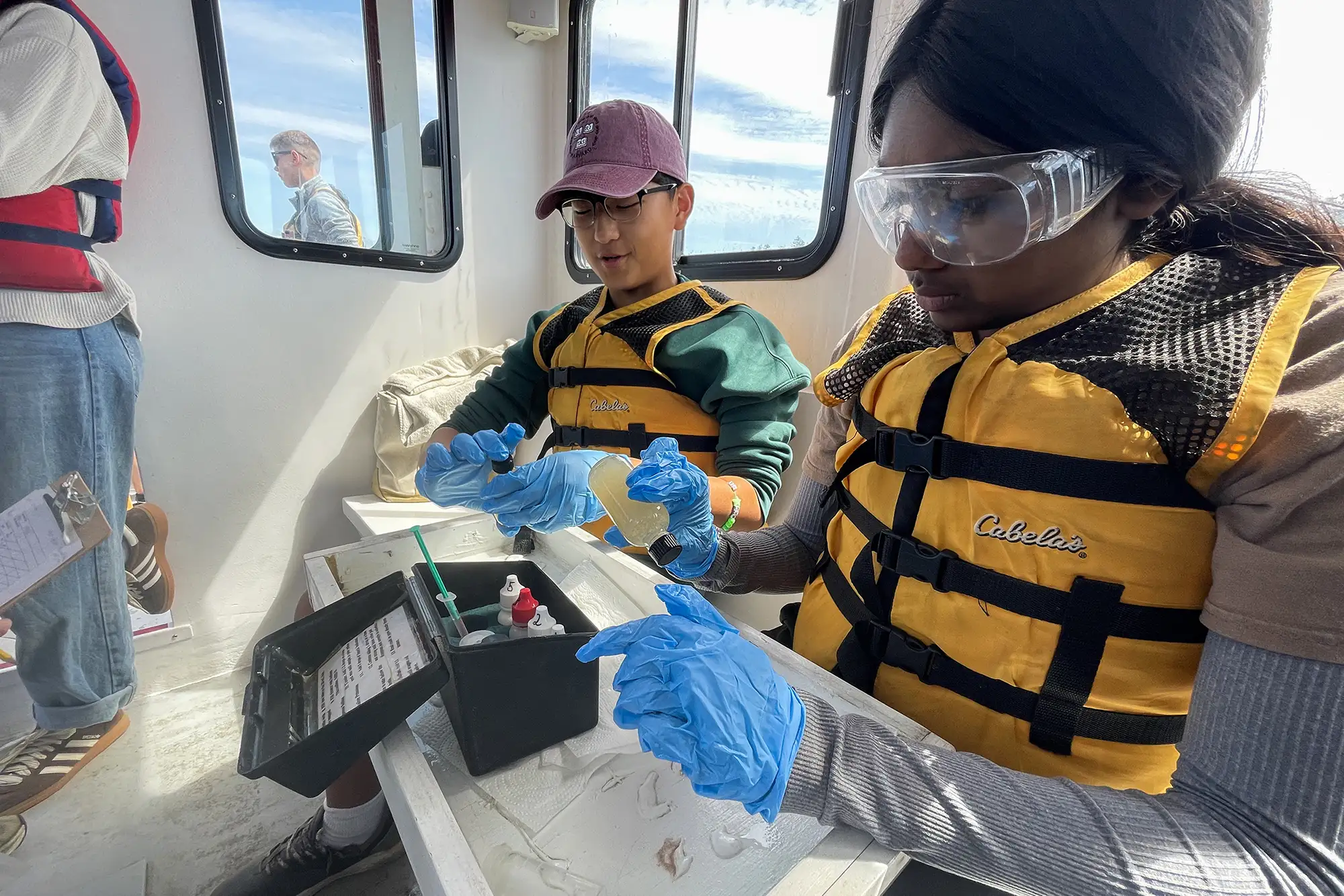 boy-girl-testing-samples-on-boat A boy and girl wearing life vests and goggles testing water samples on a boat