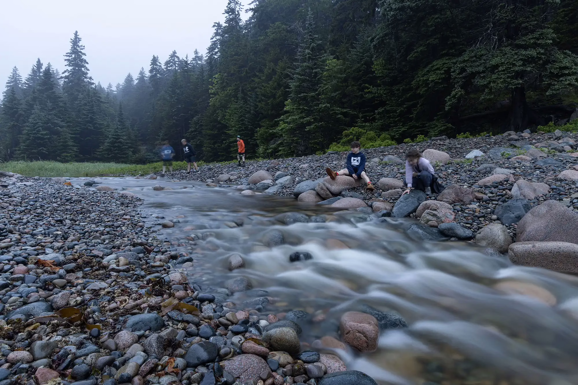 water-over-rocks Water flowing over beach rocks in the foreground, campers in the background with large evergreen trees in the distance